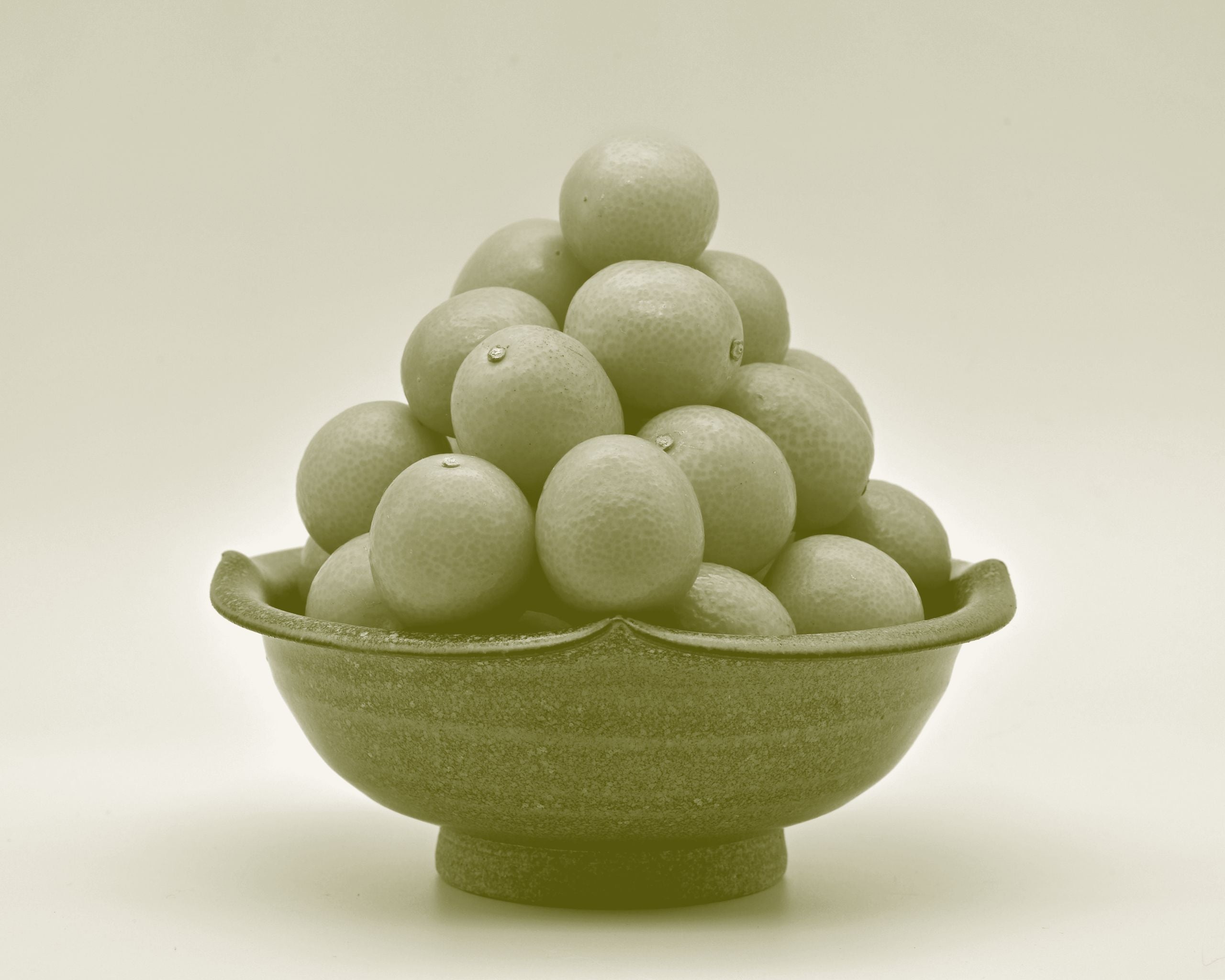 Whole cumquats stacked in a ceramic bowl, their small oval form and glossy skins catching the light.